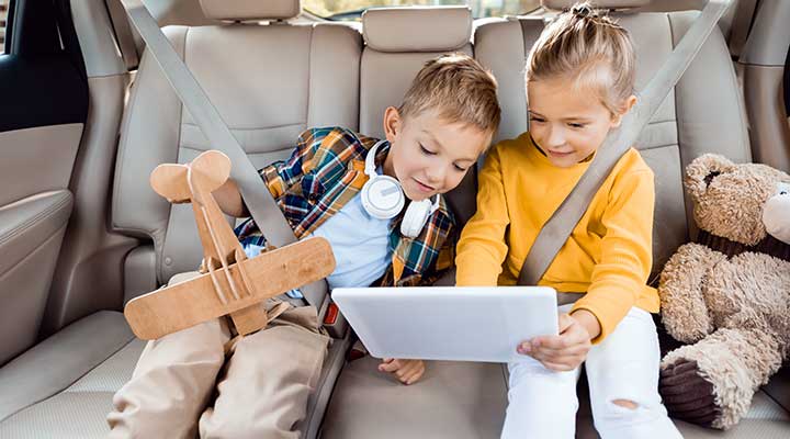 two kids in backseat of car stay entertained on a road trip with tablet and toys